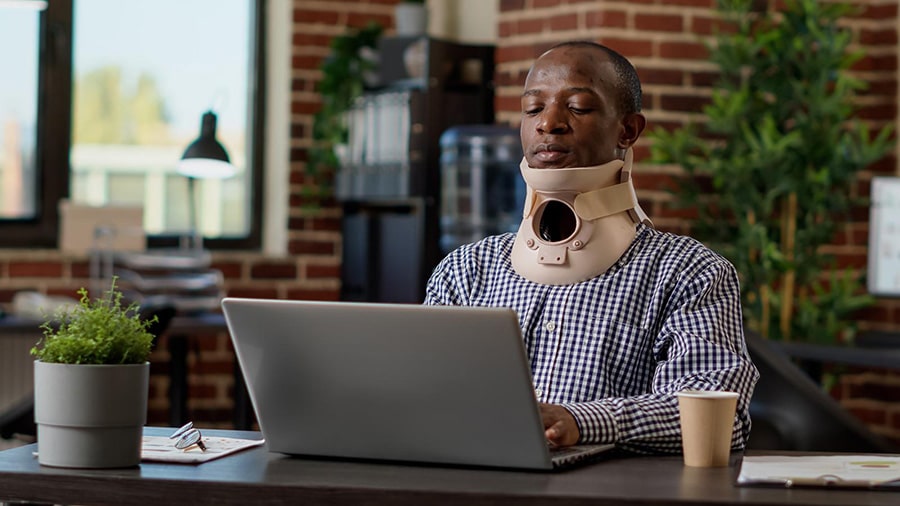 Man wearing a neck brace while typing on a laptop