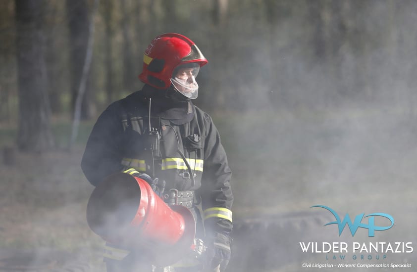 Firefighter holding a water hose while in full gear standing in a smoky environment