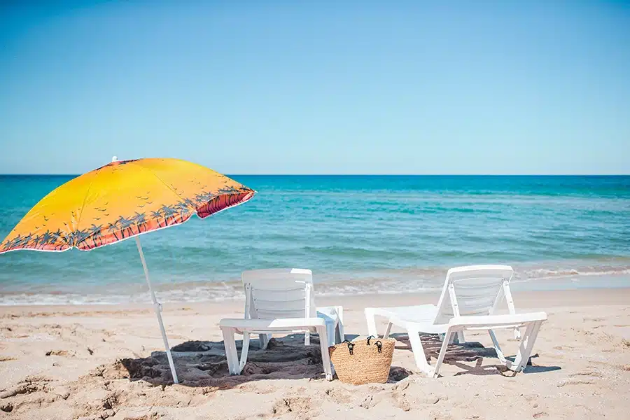 Yellow-orange umbrella on a beach with two chairs to the right of it